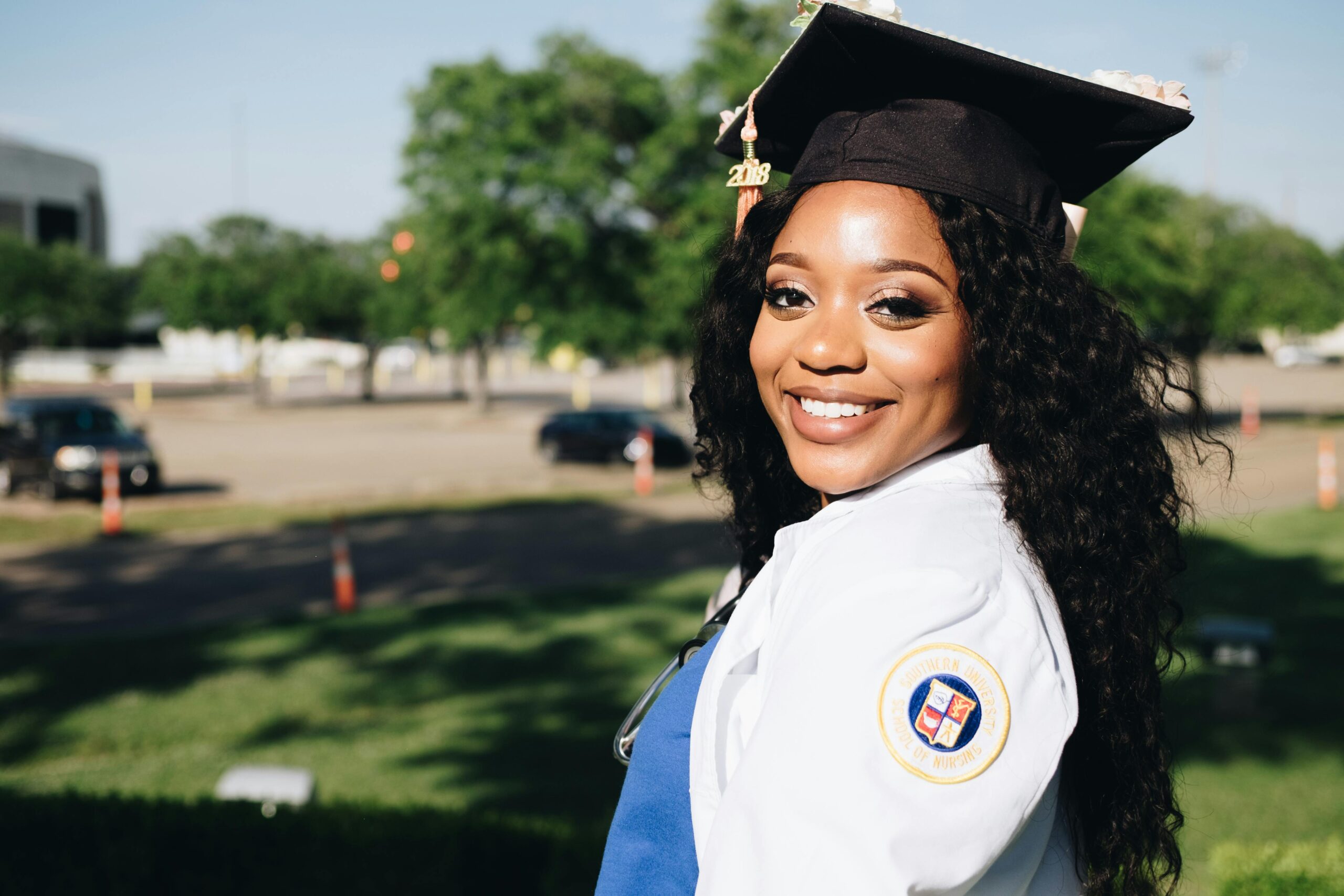 African American woman in graduation attire, smiling outdoors, symbolizing academic success.