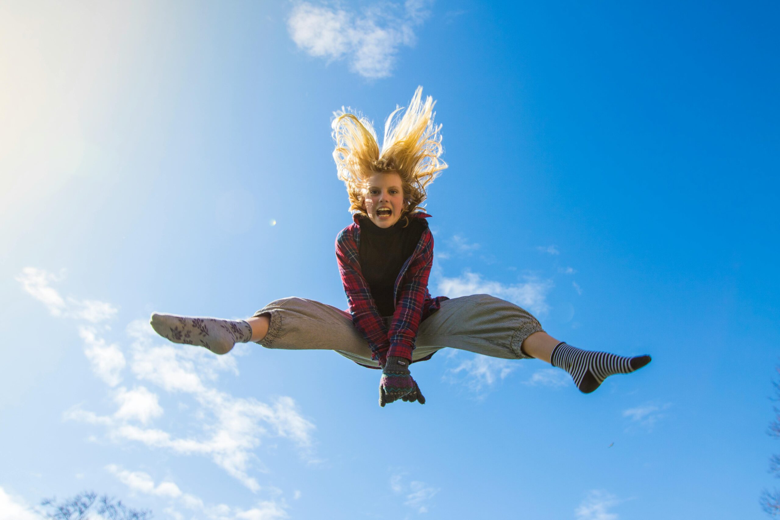 A girl energetically jumping under a clear blue sky, expressing freedom and joy.