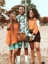 Happy young African American friends gathering together on sandy beach and embracing each other while looking at camera with toothy smiles